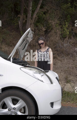 Eine junge Frau sieht ihr Auto bei geöffneter Motorhaube besorgt. Stockfoto