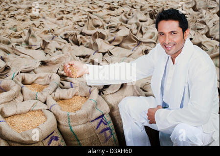 Man sitzt in der Nähe von Säcke Weizen und zeigt Weizenkörner, Anaj Mandi, Kapur, Gurgaon, Haryana, Indien Stockfoto