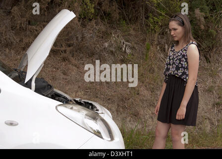 Eine junge Frau steht wieder aus ihrem Auto mit der Motorhaube auf und schaut besorgt. Stockfoto