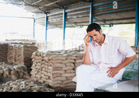 Betonte Mann sitzt auf einem Stapel von Säcken in Lager, Anaj Mandi, Kapur, Gurgaon, Haryana, Indien Stockfoto