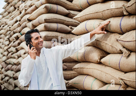 Mann stand in der Nähe Säcke Weizen und sprechen auf einem Handy Anaj Mandi, Kapur, Gurgaon, Haryana, Indien Stockfoto