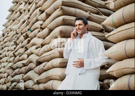 Mann stand in der Nähe Säcke Weizen und sprechen auf einem Handy Anaj Mandi, Kapur, Gurgaon, Haryana, Indien Stockfoto