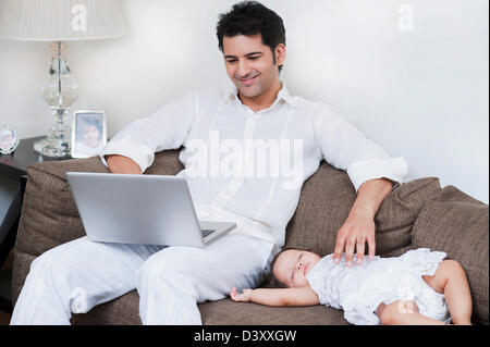 Mann mit seiner Tochter, die neben ihm schlafen auf einem Laptop arbeitet Stockfoto