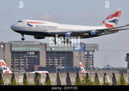 British Airways 747, das in Heathrow landet, überquert den Wartungshangar der British Airways mit anderen BA-Flugzeughängen Stockfoto