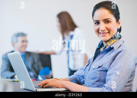 Porträt von eine Geschäftsfrau, die mit ihren Kollegen im Hintergrund auf einem Laptop arbeiten Stockfoto