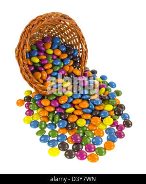 Einen kleinen Weidenkorb auf die Seite mit bunt gestrichenen Pralinen Verschütten auf einem weißen Hintergrund. Stockfoto