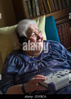 Ältere Dame hören Sie ein Hörbuch mit einem CD-Spieler, die zur Verwendung durch harte schwerhörig, blind oder visuell beeinträchtigte Menschen Stockfoto