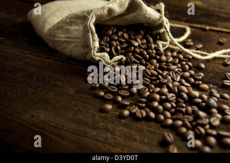 Jute Beutel gefüllt mit Kaffeebohnen auf dunklen Holzbrett, selektiven Fokus Stockfoto