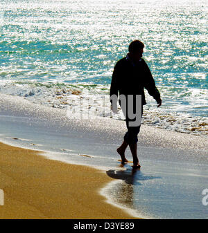 Ein Mann barfuß entlang der Küstenlinie von einem Sandstrand entfernt. Stockfoto