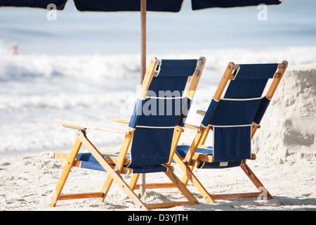 zwei Luxus-Strandkörbe sitzen unter einem Regenschirm am sonnigen Strand Stockfoto