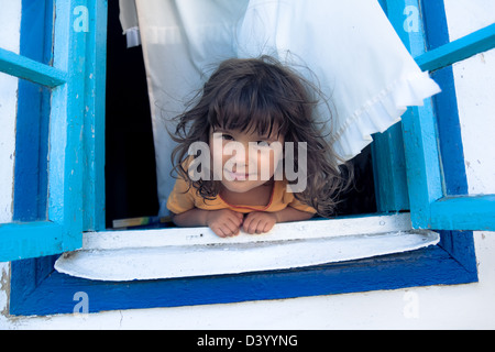 Lächelndes Mädchen auf der Suche von einem blauen Fenster mit weißen Gardinen. Stockfoto