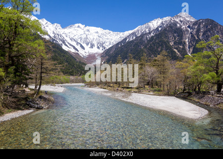 Das kühle klare Wasser des der Azusa-Fluss, der durch die Bäume an Kamikochi mit Japans Norden der Alpen im Hintergrund. Stockfoto