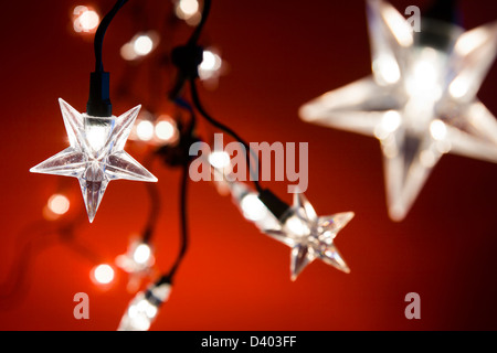 Linie der Sterne geformt Weihnachtsbeleuchtung vor einem roten Hintergrund, engen Schärfentiefe. Stockfoto