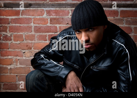 Gefährlich aussehenden Mann in schwarz gekleidet, in der Nähe einer Mauer sitzen. Stockfoto