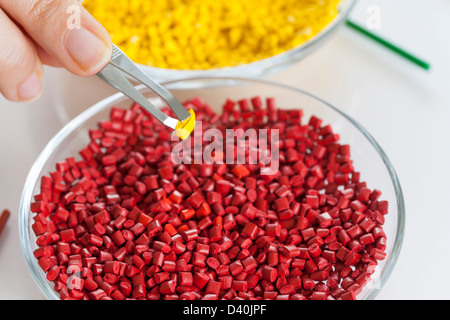 Rote und gelbe Kunststoff Masterbatch Granulat von einer Pinzette genommen Stockfoto