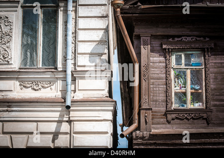 Zwei Häuser verschiedenen Stils in Russland. Alte dunkle Holzhaus mit geschnitzten Fenster und weiße Backsteinhaus mit Stuckarbeiten. Tradit Stockfoto