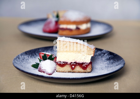 Eine Victoria Biskuit Erdbeer-Marmelade auf einem Teller mit Sahne Erdbeeren und einer Prise Puderzucker Stockfoto