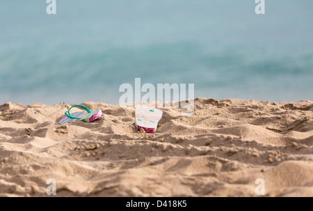 Ausrangierte Childs Flip-Flops am Sandstrand vom türkisblauen Ozean in Sonne Stockfoto