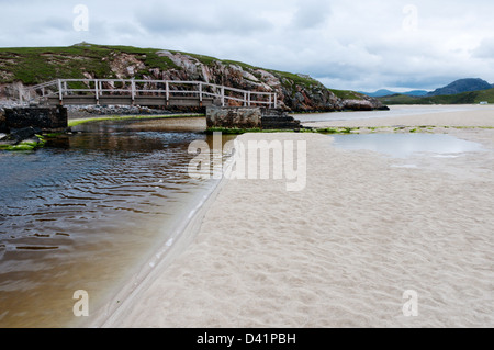Eine Fußgängerbrücke über einen kleinen Bach auf den Sandstrand bei Ebbe am Tràigh Ùige auf der Isle of Lewis auf den äußeren Hebriden. Stockfoto