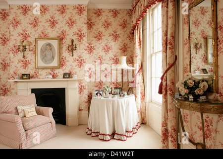 Weißes Tuch auf den Tisch in der Ecke von Reihenhaus Schlafzimmer mit rosa Sessel und rosa geblümte Tapete Stockfoto