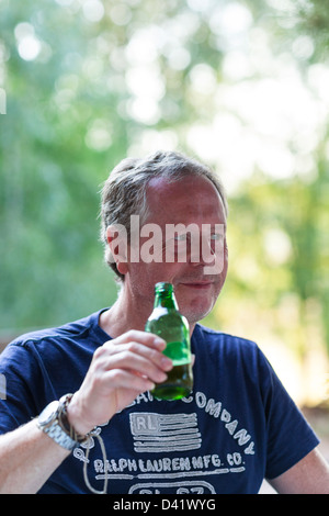 An einem heißen Sommertag entspannt ein Mann draußen im Schatten durch das Trinken einer Flasche Bier. Stockfoto