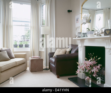 Braun Ledersessel am Kamin im Wohnzimmer Stadthaus mit Sahne Sofa neben Fenster mit weißen Gardinen Stockfoto