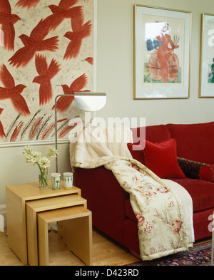 Großes Bild von roten Vögel im Flug über hellem Holz Verschachteln von Tabellen im modernen Wohnzimmer mit floralen Wurf auf roten sofa Stockfoto