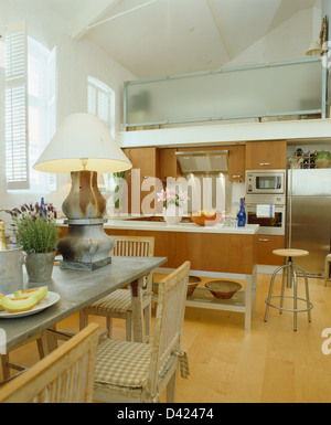 Beleuchtete Lampe auf Zink-Spitze Tisch mit Holzstühlen im modernen Küche Esszimmer im Studio-Apartment mit Holzboden Stockfoto
