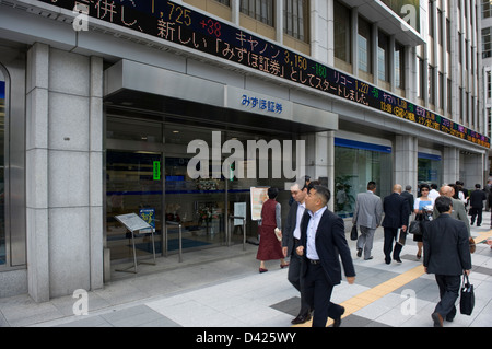 Geschäftsleute und Fußgänger zu Fuß vorbei an elektronische Börse Ticker Tape auf Wertpapiergeschäfte in der Innenstadt von Tokio, Japan. Stockfoto