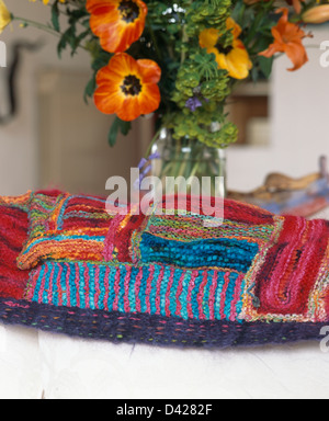 Nahaufnahme von bunten handgestrickte Patchwork Wurf aus handgefertigten Garne neben Vase mit orangen Blüten hergestellt Stockfoto