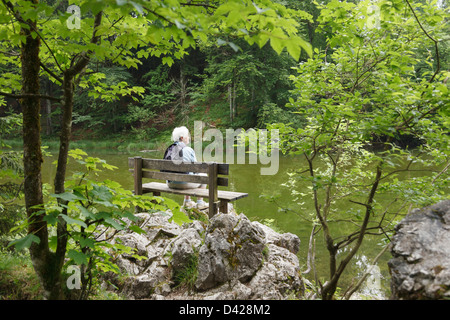 Ältere Frau ruhig alleine sitzen auf einer Bank im Regen in der ruhigen und friedlichen Umgebung von taubensee See Ruhpolding Chiemgau Bayern Deutschland Stockfoto