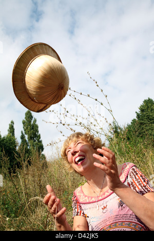 Berlin, Deutschland, sitzt eine Frau auf einer Wiese, lachen und werfen ihren Hut in der Luft Stockfoto