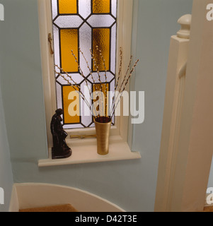 Orange-weiße Glasfenster mit Skulptur und Willow Zweige in Vase auf Fensterbank Stockfoto