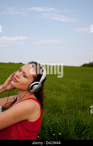 Freiburg, Deutschland, eine junge Frau sitzt in einer Wiese und hört Musik Stockfoto