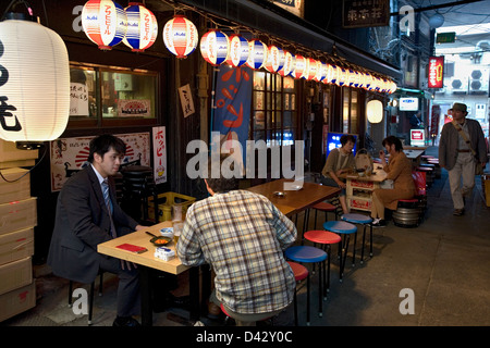 Gönner mit Bier und Brotzeit am Bürgersteig Izakaya trinken Einrichtung versteckt unter der Hochbahn in Okachimachi, Tokio Stockfoto