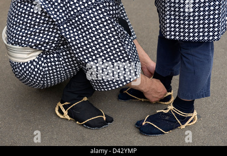 Zwei Sanja Matsuri Festival Teilnehmer beenden für einen Moment ihre Waraji Stroh Sandalen in Asakusa, Tokio anpassen. Stockfoto