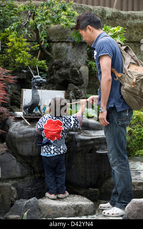Ein Vater hilft seinem Sohn die Temizuya Brunnen für das Waschen der Hände und Mund vor dem Eintritt in einen Schrein in Japan zu erreichen. Stockfoto