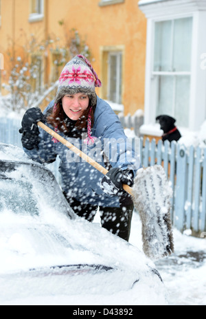 Eine Autofahrer löscht Schnee aus ihrem Auto in das Dorf von Badminton Gloucestershire UK Stockfoto