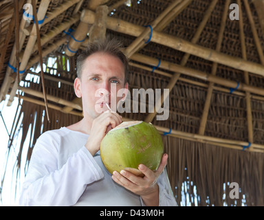 attraktiver Mann trinkt Cocossaft aus einer Nuss Stockfoto