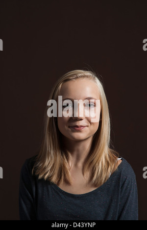 Porträt von Blond, Teenager-Mädchen, lächelnd in die Kamera, Studio Shot auf schwarzem Hintergrund Stockfoto