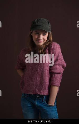 Porträt von Blond, Teenager Mädchen lächelnd in die Kamera mit Hand in der Tasche tragen Baseball-Mütze, Studioaufnahme auf schwarzen Hintergrund Stockfoto