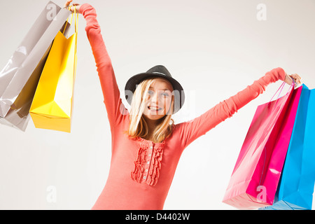 Low Winkel Ansicht Porträt von Blond, Teenager-Mädchen Hut trägt und hält Einkaufstaschen in Luft, Studioaufnahme auf weißem Hintergrund Stockfoto