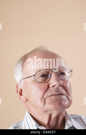 Porträt von Senior Mann mit Brille und blickte in die Ferne mit betroffenen Ausdruck auf Beige Hintergrund Stockfoto