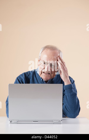 Senior Mann sitzen sitzen am Tisch mit Laptop-Computer schauen verwirrt, Studioaufnahme auf Beige Hintergrund Stockfoto