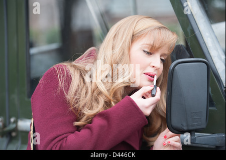Frau gilt Lippenstift in Autospiegel Stockfoto
