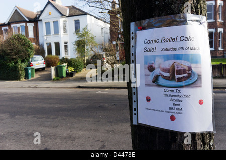 Ein Schild an einem Baum in einer Vorstadt Straße angeheftet wirbt einen Verkauf von Kuchen zugunsten von Comic Relief Stockfoto