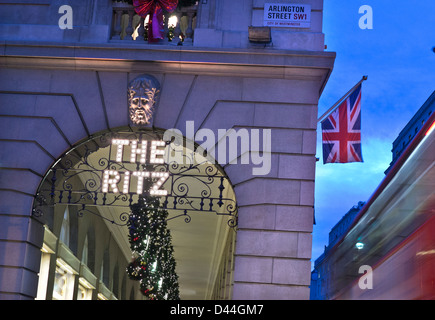 Das Ritz Hotel London bei Dämmerung Außenleuchten name mit Weihnachtsschmuck Union Jack Flagge und verschwommenes vorbei an roten Bus Piccadilly London UK Stockfoto