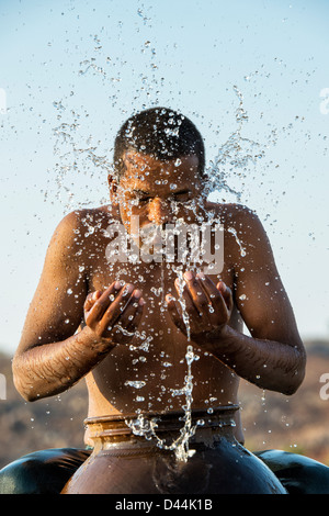 Indischer Mann Spritzwasser über sich selbst aus einem Wassertopf bei Sonnenuntergang. Indien Stockfoto