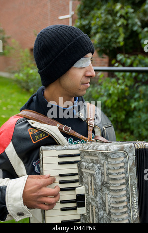 Ein Zigeunerjunge mit einem beschädigten Auge spielt Akkordeon und betteln. Stockfoto