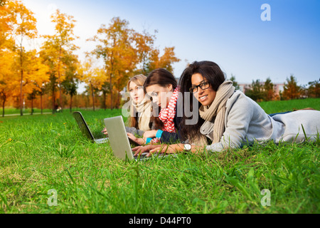 drei Schülerinnen und Schüler mit Laptops in den Park verlegen Stockfoto